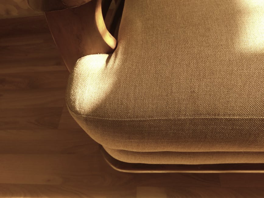 Close-up view of a beige upholstered armchair in a living room during surface cleaning, showing the fabric seat and rounded armrest. The fabric appears clean and well-maintained, with a firm and smoot