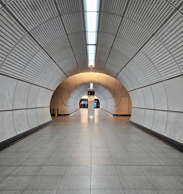 A clean and well-lit platform at Canonbury Station, showing smooth, polished tiles with clear directional markings and a white tactile strip along the edge. The underground tunnel features a curved ce